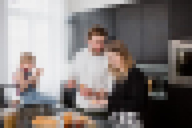 Couple cooking in a modern kitchen with a child in the background taking a photo.